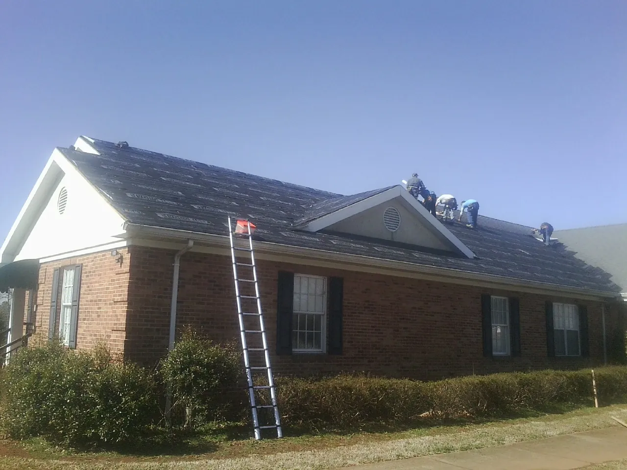 Crew tearing shingles off a brick ranch roof with a ladder set — Metal Roof Repair work by our crew in Garnet Valley