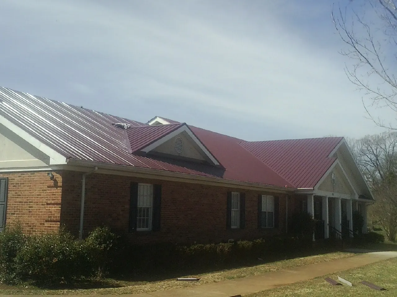 Red metal roof with gabled entries on a long brick building, from a Hail Damage Roof Repair job in Garnet Valley