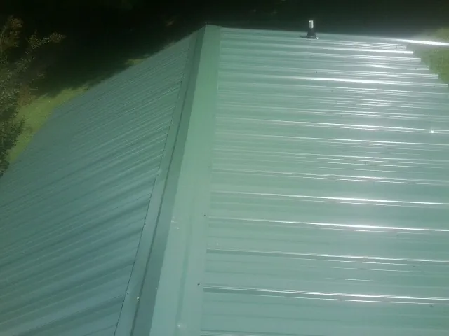 New green metal panels meeting at the ridge of a roof — Flat Roof Repair work by our crew in Garnet Valley