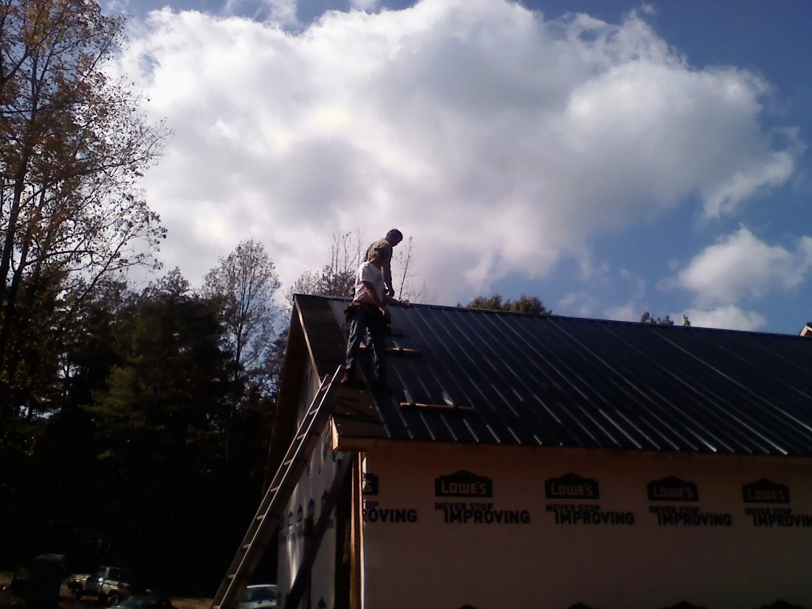 Roofer fastening dark metal panels high against a cloudy sky, from a Roof Inspection job in Garnet Valley