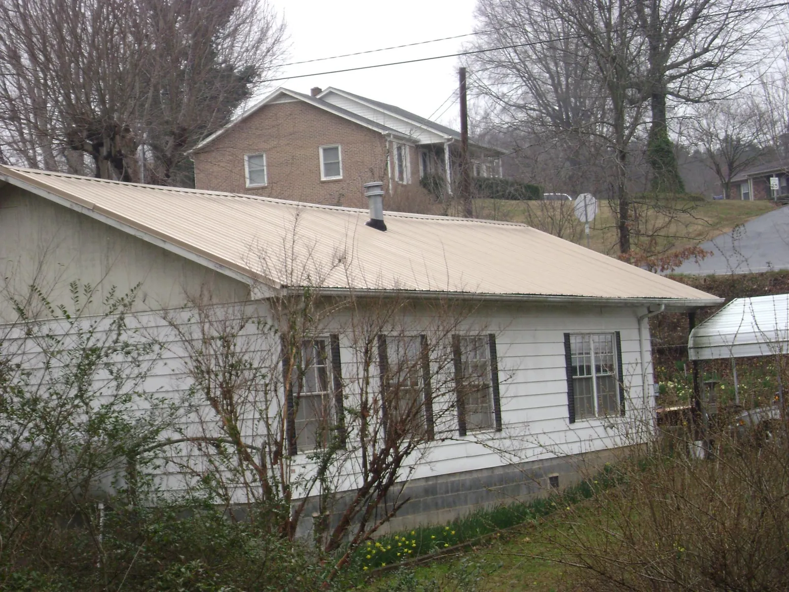 Tan metal roof on a white sided house set into a hillside — Commercial Roofing by Roofing Brothers in Garnet Valley
